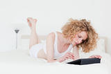 Charming blonde woman relaxing with her tablet while lying on a 