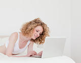 Attractive blonde woman relaxing with her laptop while lying on 