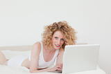 Charming blonde woman relaxing with her laptop while lying on he
