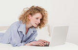 Gorgeous blonde woman relaxing with her laptop while lying on he