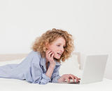 Beautiful blonde female relaxing with her laptop while lying on 