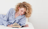 Gorgeous blonde woman reading a book while lying on her bed