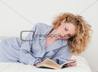 Beautiful blonde woman reading a book while lying on her bed