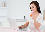 Brunette using her laptop and drinking orange juice