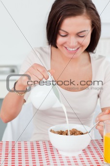 Beautiful dark-haired woman pouring milk in her cereal