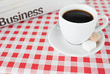 A cup of coffee and a newspaper on a tablecloth
