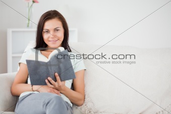 Cute dark-haired woman holding a book while looking at the camer