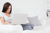 Close up of a young brunette sitting on a sofa using a laptop