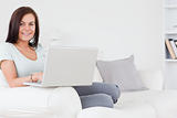 Close up of a charming brunette sitting on a sofa using a laptop