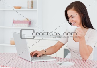 Charming woman using her laptop and having a tea