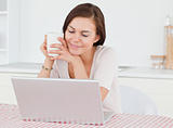 Cute dark-haired woman using her laptop and having a tea