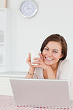 Smiling dark-haired woman using her laptop and having a tea