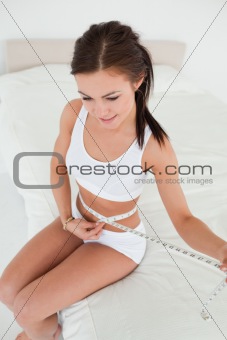 Young woman sitting on her bed to measure her belly