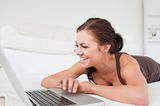 Smiling woman lying on a carpet with a laptop
