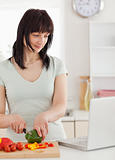 Attractive brunette woman cooking while relaxing with her laptop