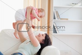 Charming woman holding her baby in her arms while sitting on a s