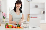 Smiling brunette woman cooking while relaxing with her laptop