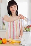 Charming brunette woman putting vegetables in a mixer while stan