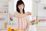 Pretty brunette woman putting vegetables in a mixer while standi