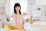Cute brunette woman putting vegetables in a mixer while standing