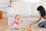 Cute woman playing with her baby in while sitting on a carpet