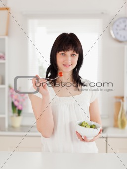 Cute brunette female eating a cherry tomato while holding a bowl