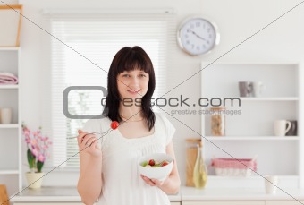 Good looking brunette female eating a cherry tomato while holdin