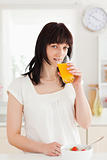Charming brunette drinking a glass of roange juice while standin