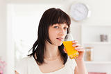 Pretty brunette drinking a glass of orange juice while standing
