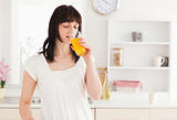 Lovely brunette drinking a glass of orange juice while standing