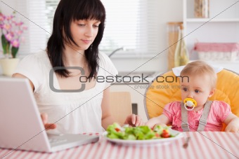 Gorgeous brunette woman eating a salad next to her baby while re