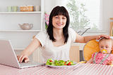 Attractive brunette woman eating a salad next to her baby while 