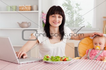 Attractive brunette woman eating a salad next to her baby while 