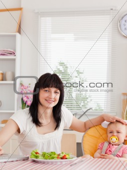 Good looking brunette woman eating a salad next to her baby whil