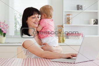 Pretty brunette woman relaxing with her laptop next to her baby 