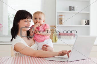 Cute brunette woman relaxing with her laptop next to her baby wh