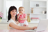 Lovely brunette woman relaxing with her laptop next to her baby 