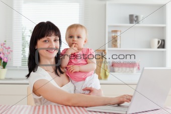 Lovely brunette woman relaxing with her laptop next to her baby 