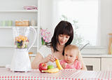 Cute brunette woman showing a banana to her baby while sitting