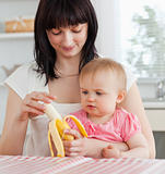 Charming brunette woman pealing a banana while holding her baby 