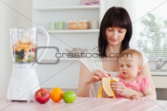 Gorgeous brunette woman pealing a banana while holding her baby 