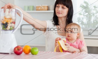 Gorgeous brunette woman putting vegetables in a mixer while hold
