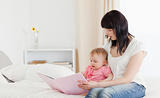 Attractive brunette woman showing a book to her baby while sitti