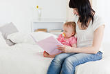 Charming brunette woman showing a book to her baby while sitting