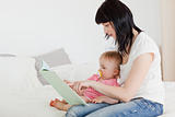 Lovely brunette woman showing a book to her baby while sitting o