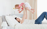 Charming brunette woman playing with her baby while lying on a b