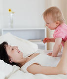 Lovely brunette woman playing with her baby while lying on a bed