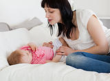 Pretty brunette female playing with her baby while lying on a be