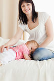 Cute brunette woman posing while her baby is lying on a bed