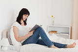 Beautiful brunette woman reading a book while sitting on a bed